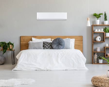 White single room heat pump mounted on a grey wall above a bed